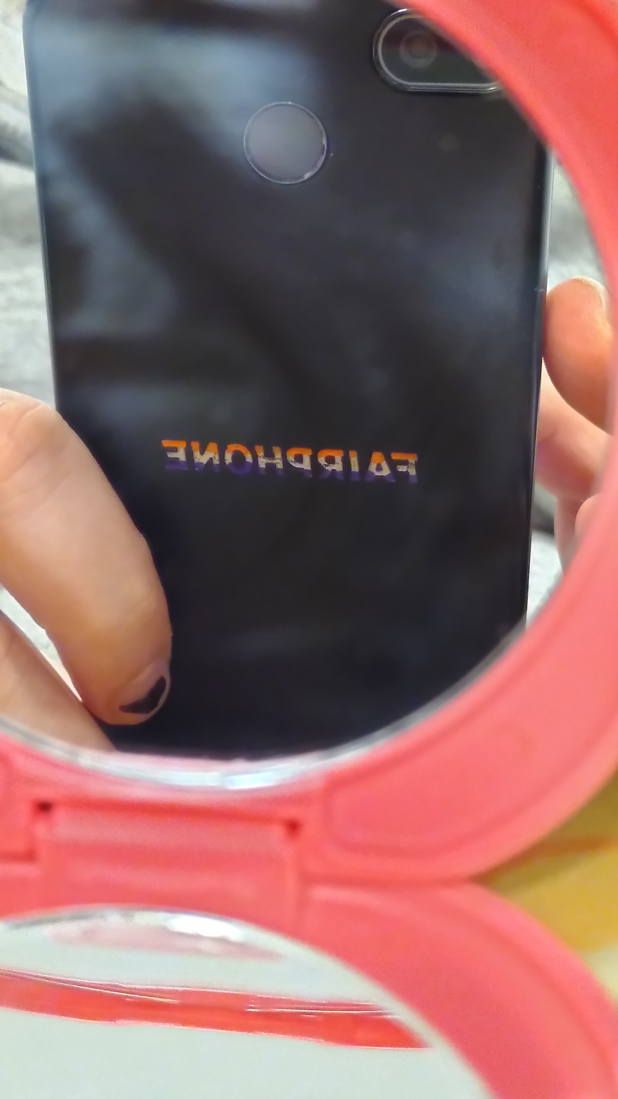 Photo of a fairphone through an hand mirror. The logo embossed on the back is filled with purple on the bottom, silver on the middle and orange on the top