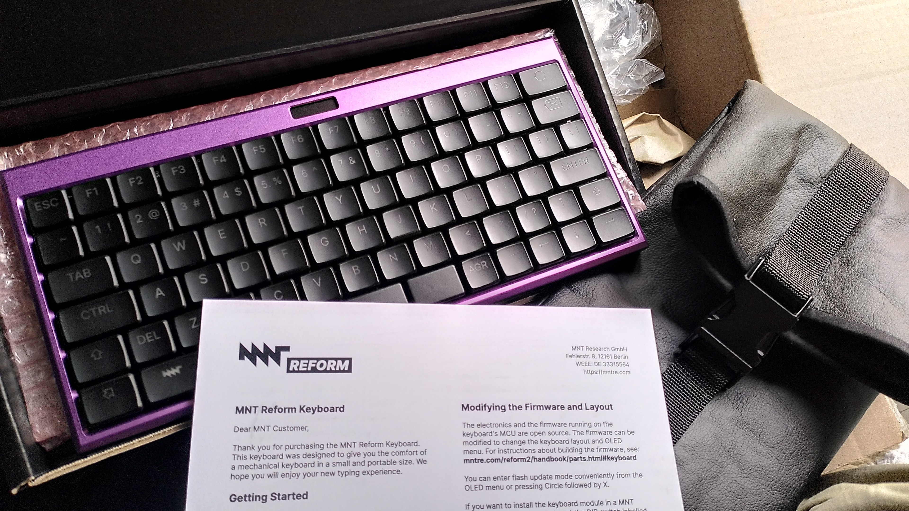 a purple MNT reform keyboard, a black vegan leather sleeve and the one page documentation