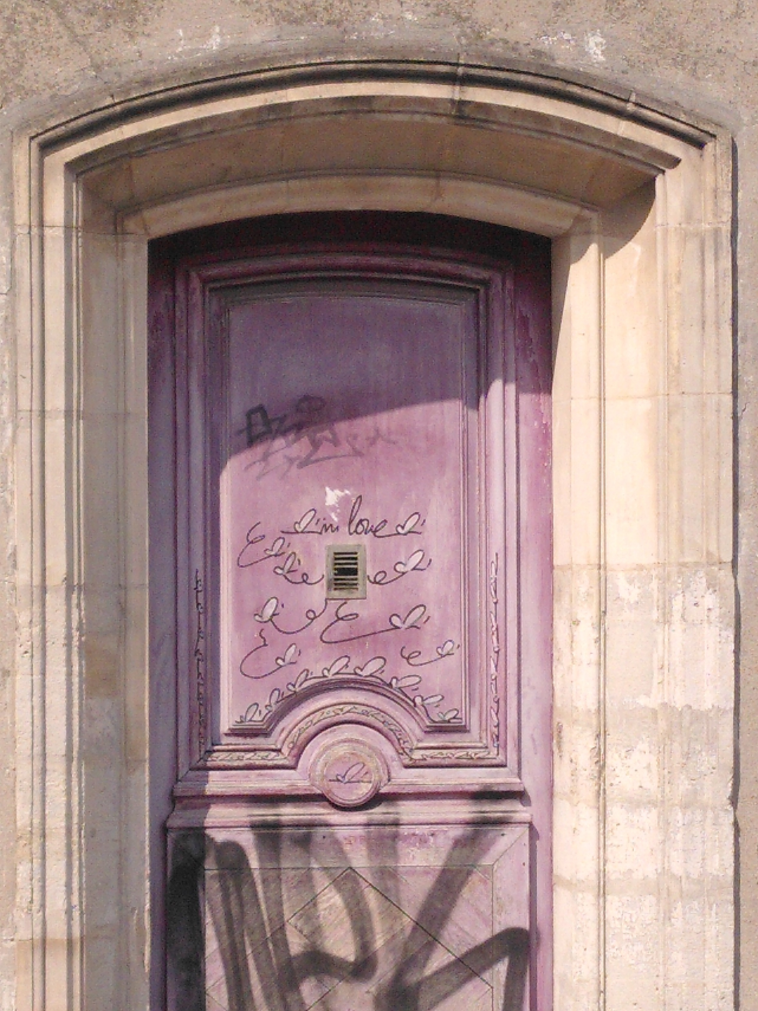 Red door set in a cream colored bas-relief, with tag. Bottom have 3 or 4 large, rough letter. Top part have many small stylized butterfly and cursive letter saying I'm love