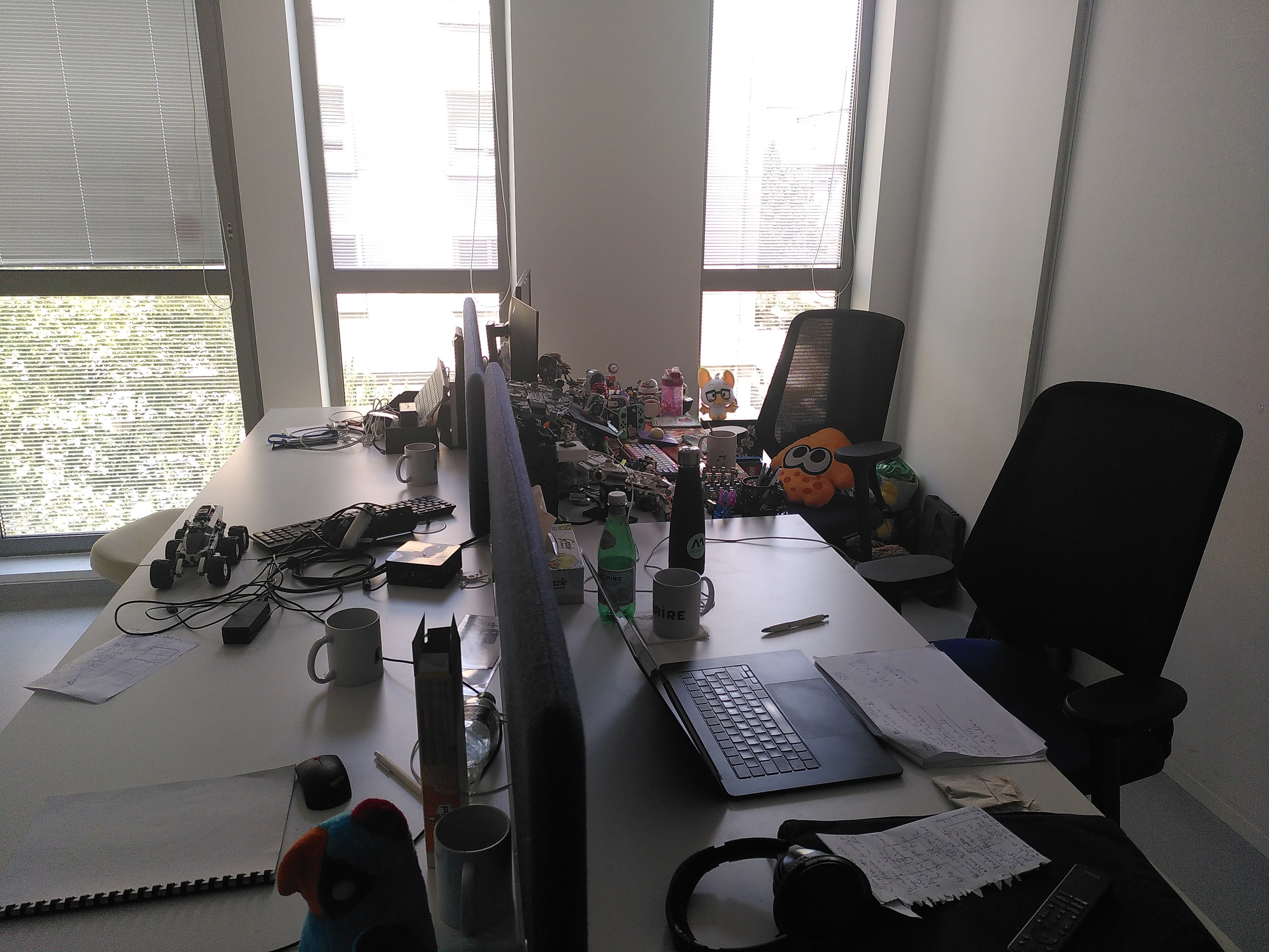 4 desks stuck together. One is covered in lego and there is a splatoon plushie sitting in a chair