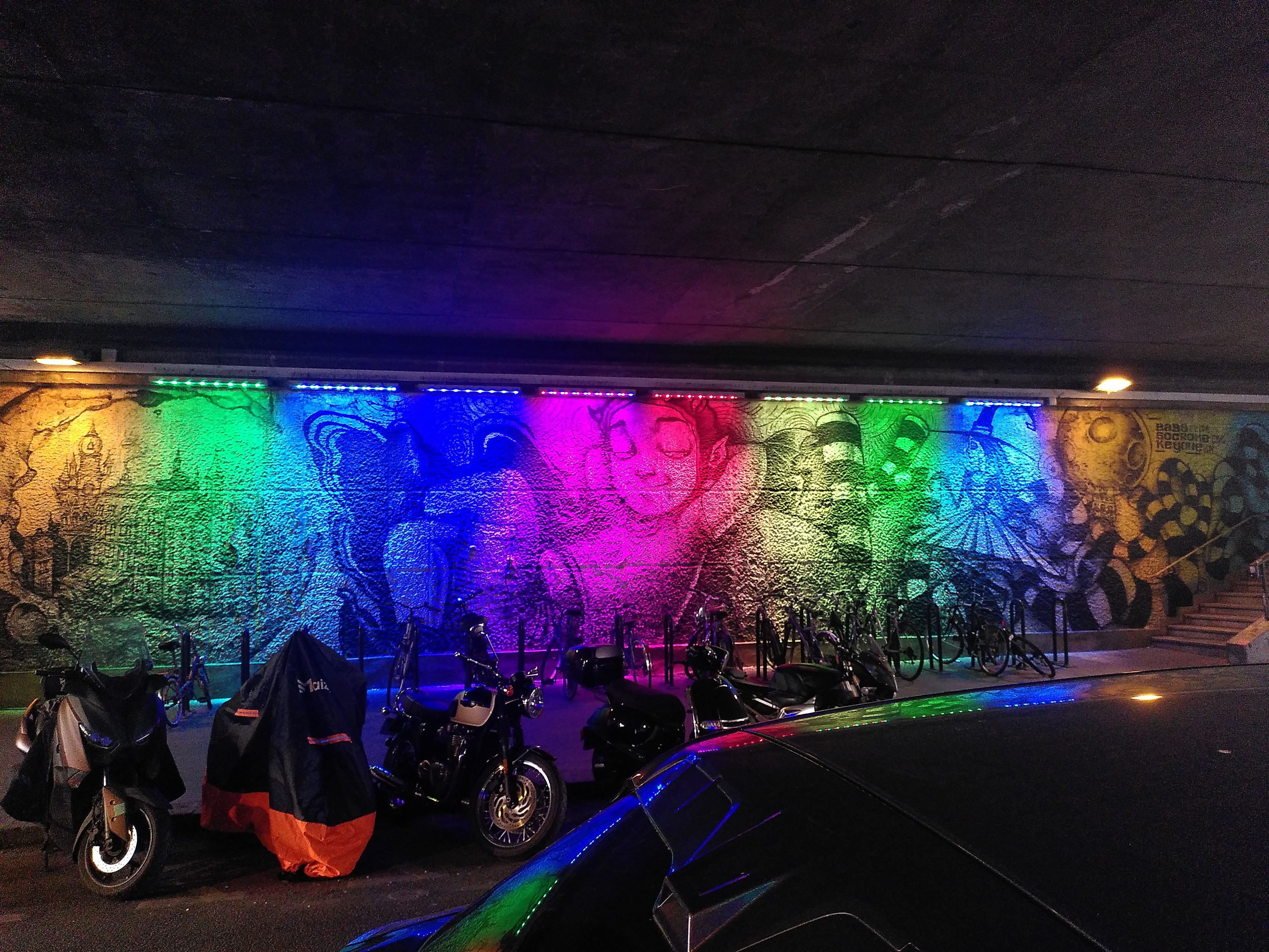 Painting on a wall under a bridge with rainbow colored lighting
