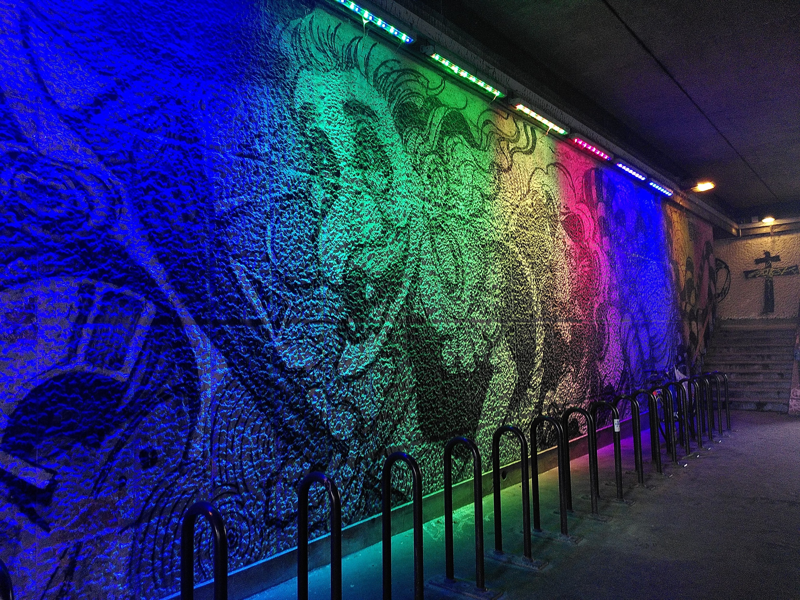 Painting on a wall under a bridge with rainbow colored lighting