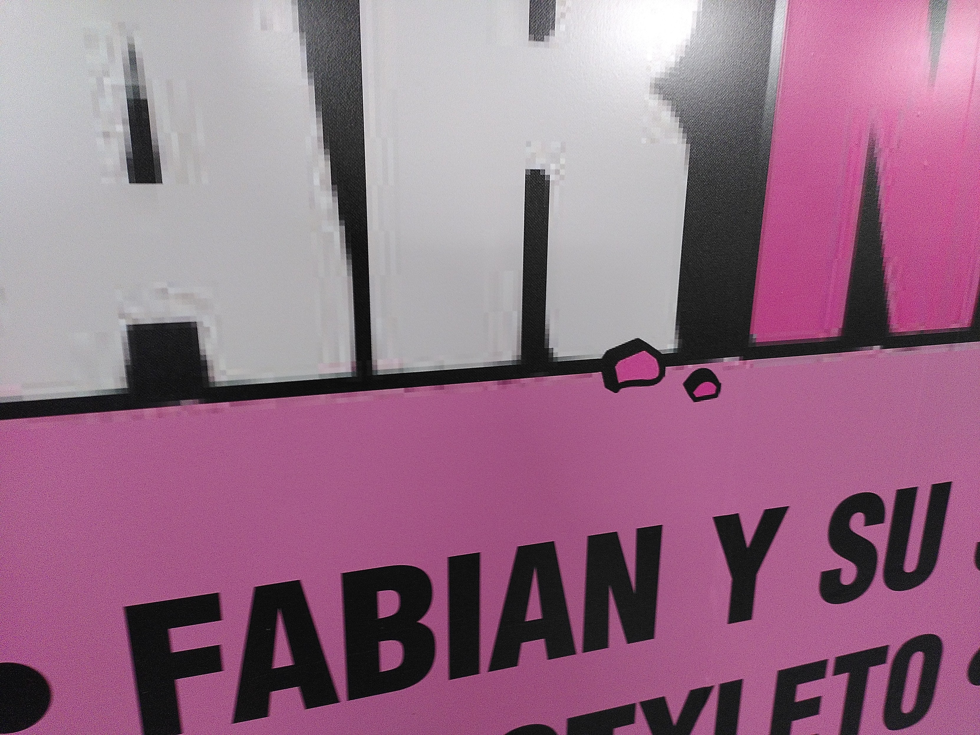 Zoom on an ads on a wall in a train station. Ads is taller than a man, very long. The zoom show the logo text have jpeg artifacts but pebbles like effect have been added with no artifacts and the text under it is perfectly crisp