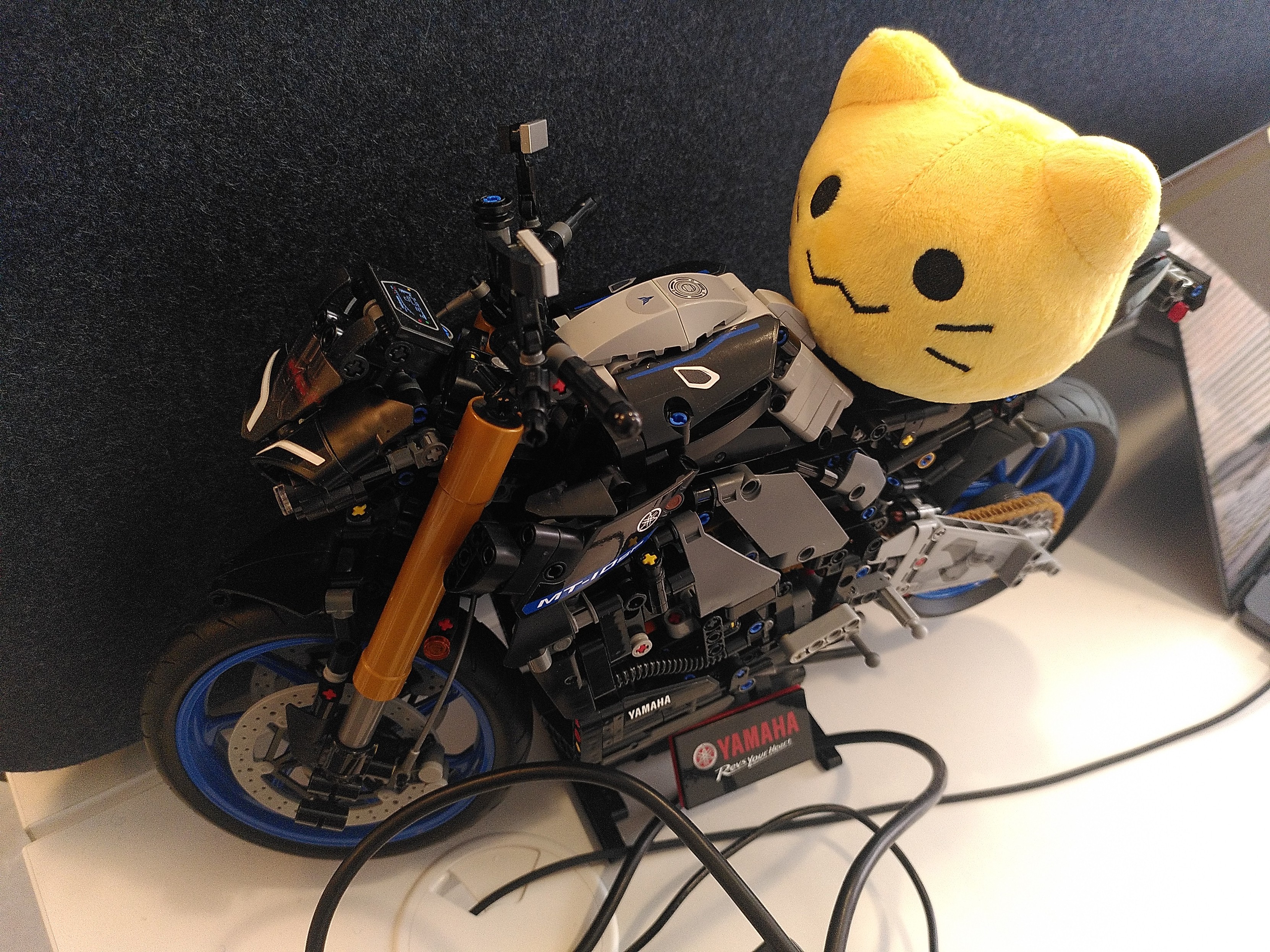 A blob cat plushie on a lego technic bike