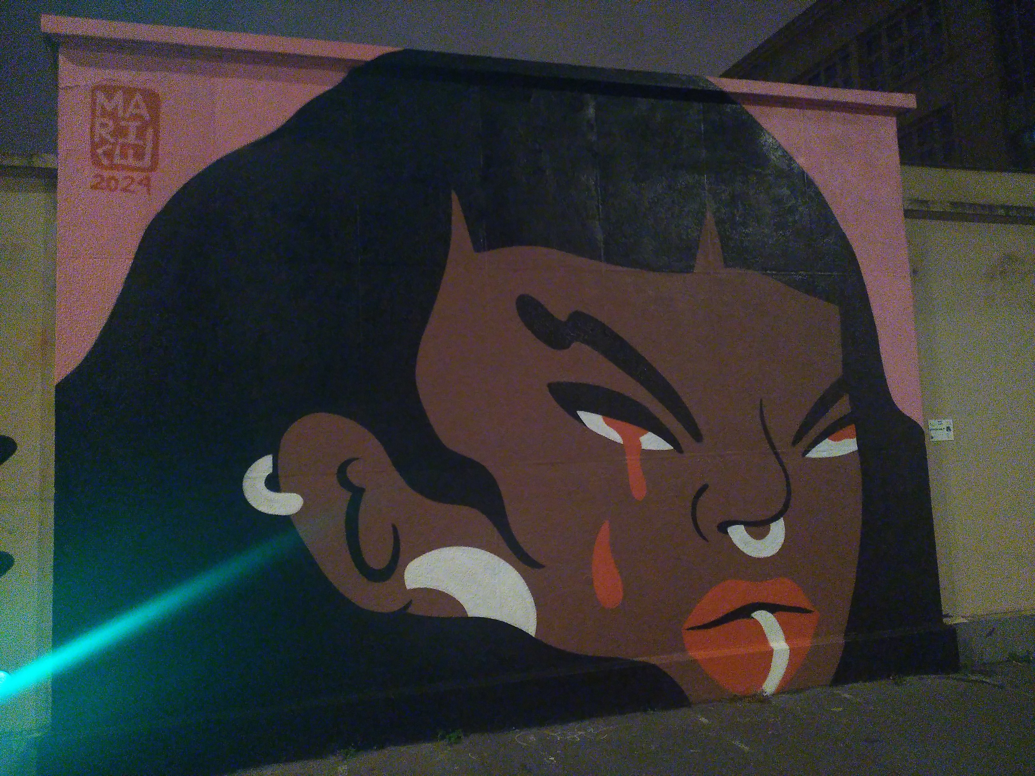 Mural painting of a black woman face with ear, nose and lower lip piercing, red pupils and right eye seem to bleed