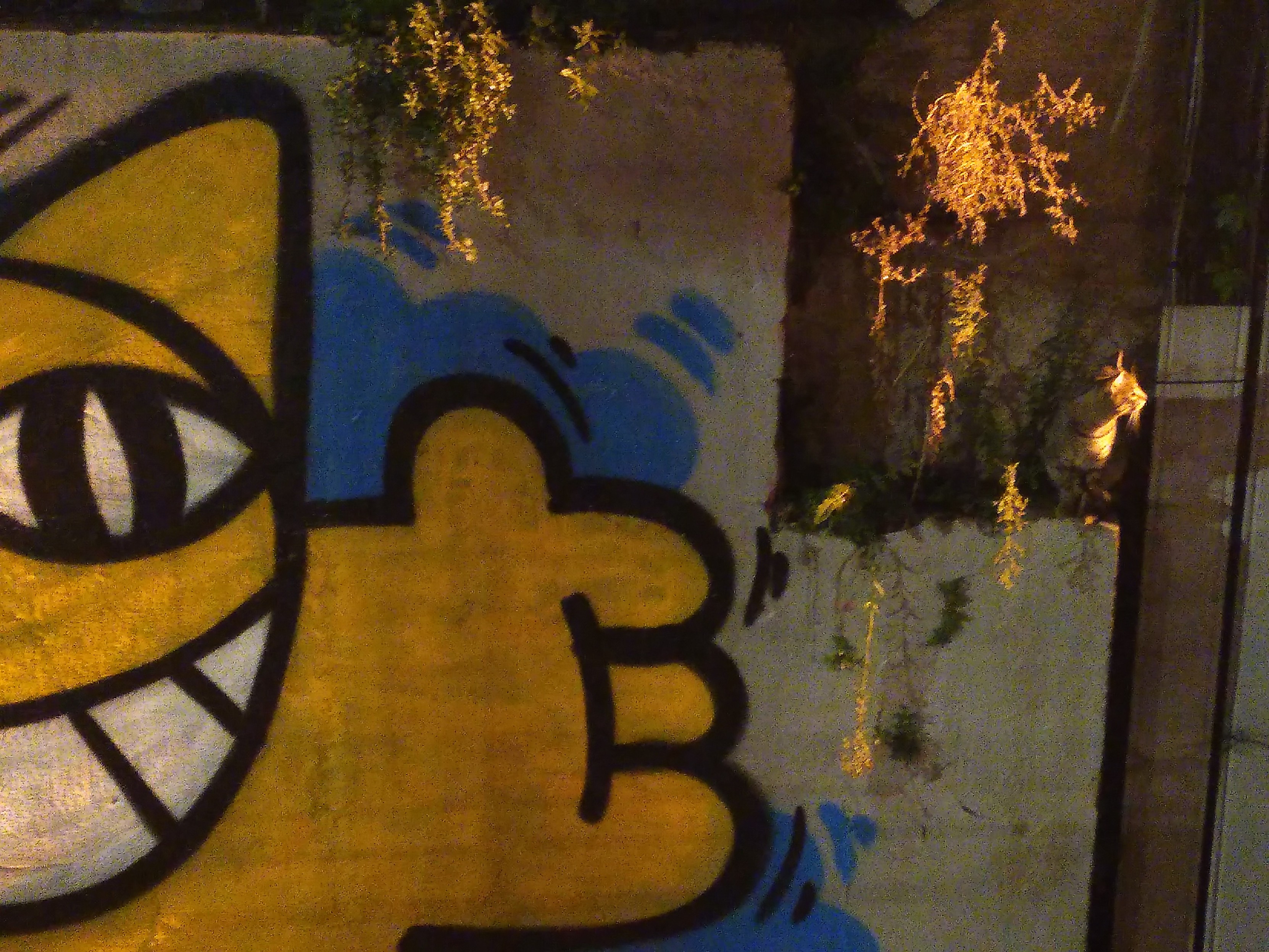 On the left, half of a large painting of a yellow cat with its arm wide open. On the right a small cat perched on a ledge