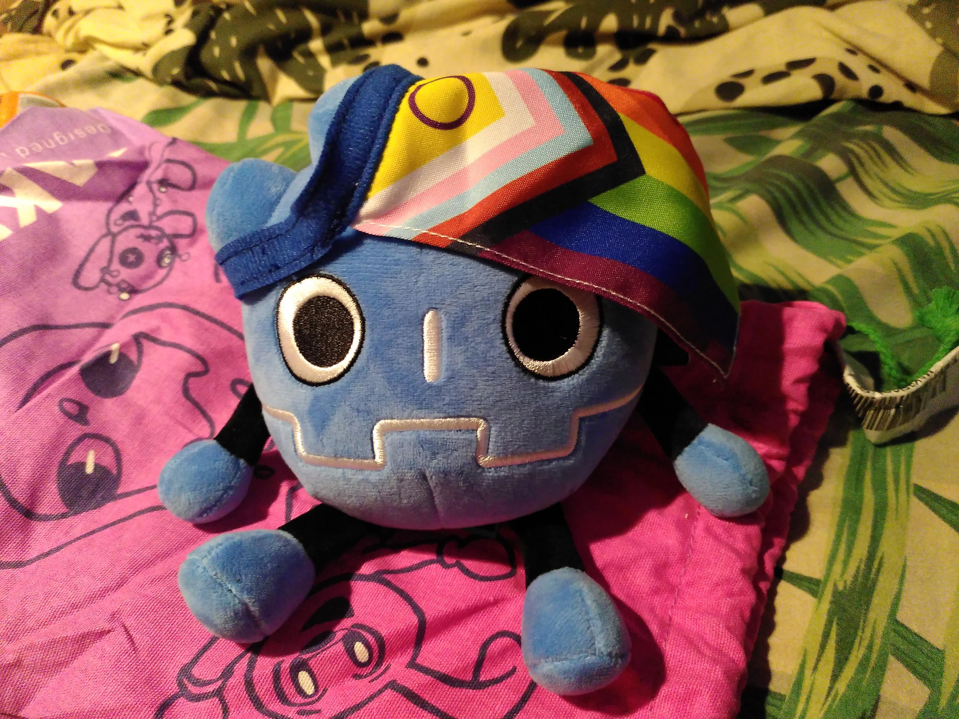 A godot plushie with a progressive rainbow flag on its head