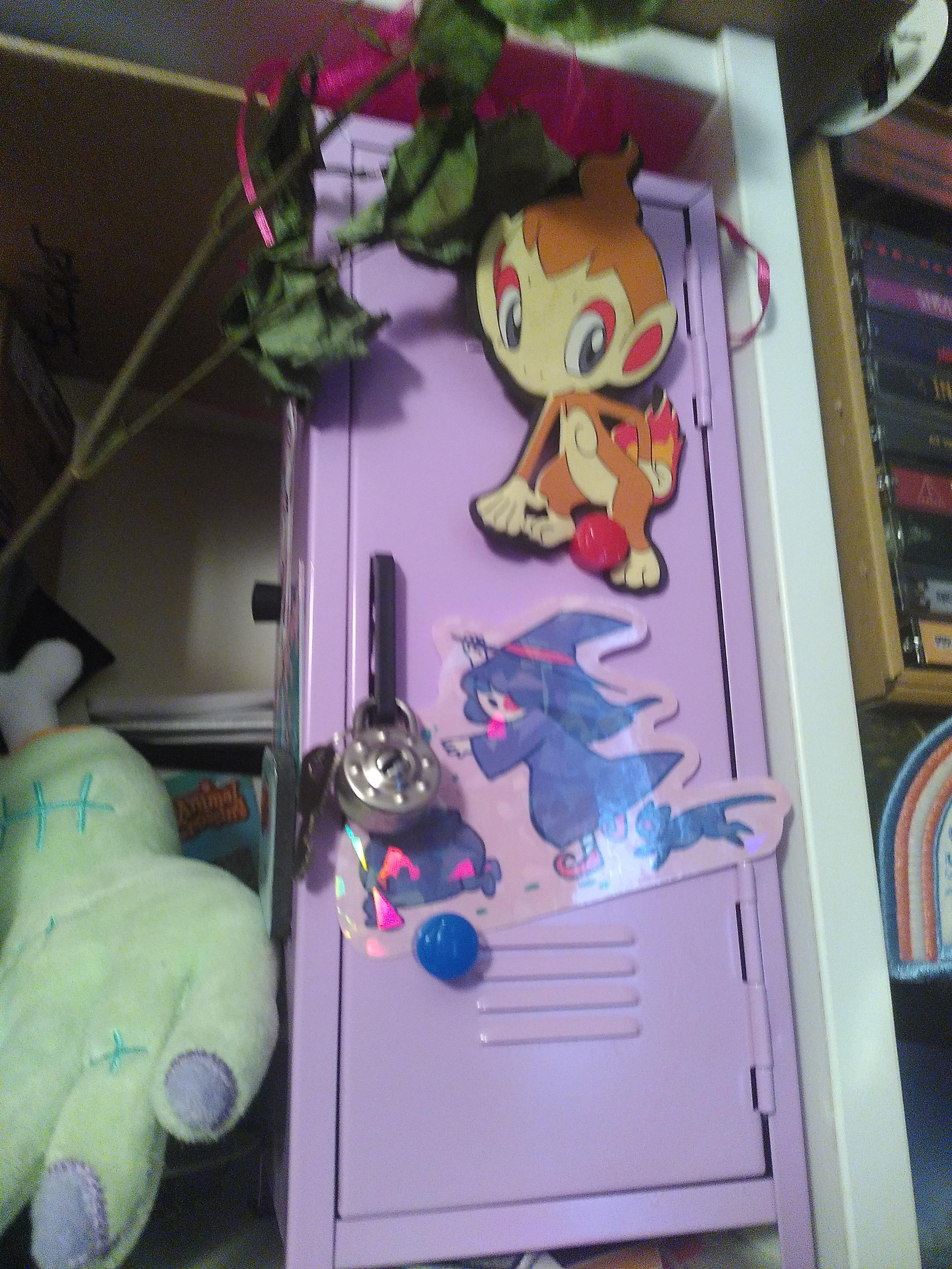 Runaway cauldron sticker. Sporting a living cauldron brewing a green liquid running away from a witch and her black kitty. It is attached with a magnet to a small pink locker. There is also a fire pokemon on the locker, a dry flower above it and a severed hand plushie on the side