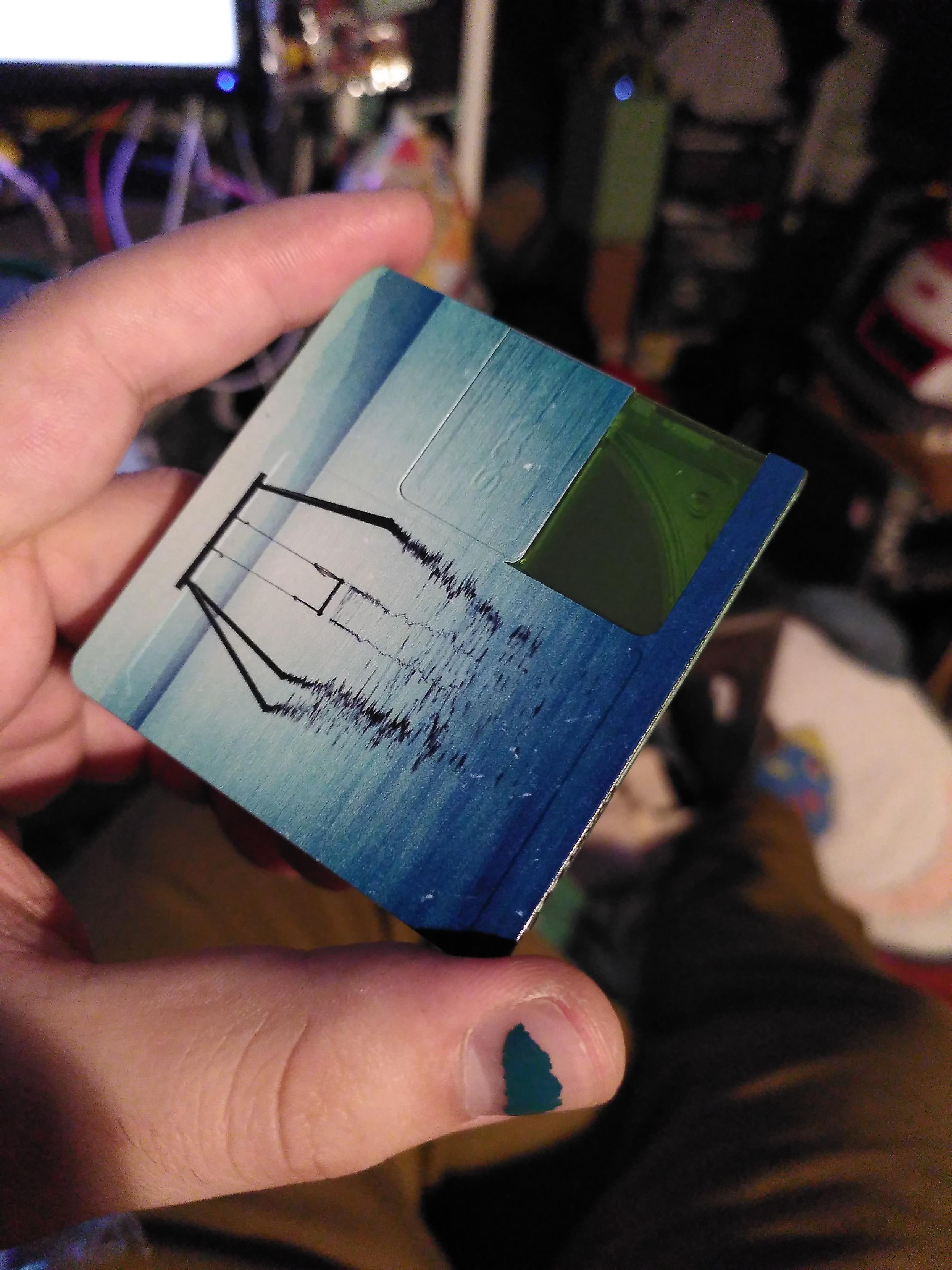 Me holding a minidisc of coleurs' Everything's temporary. This face is nearly fully printed with the album cover except where the cover slide, which is left translucent green plastic