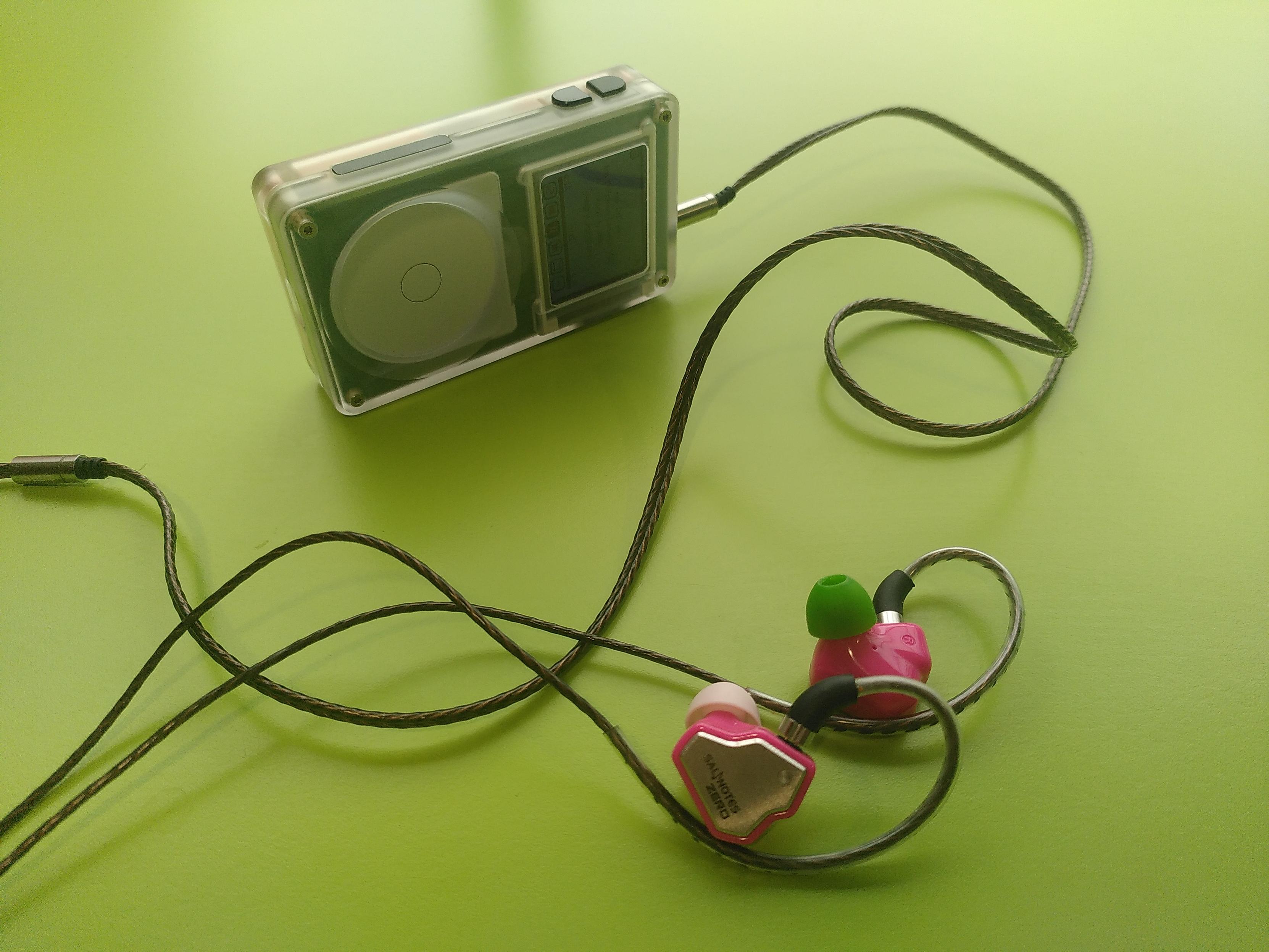 A tangara music player laying on its side on a green table. It is connected to a pair of rose salnotes zero

