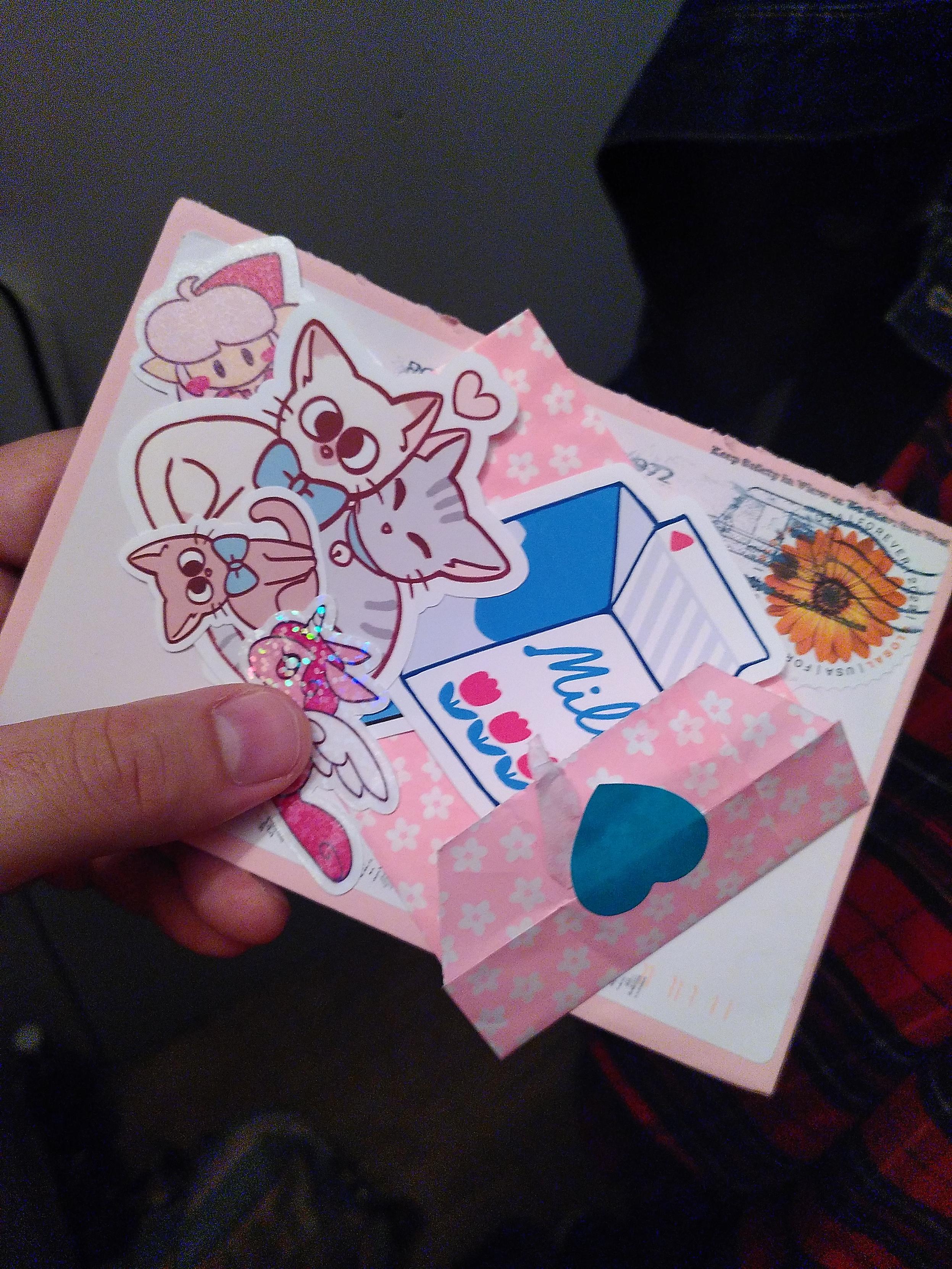 A pink envelope with a bunch of stickers. A carton of milk, a bunch of kitty, a shiny dragon and a pink hero of the legend