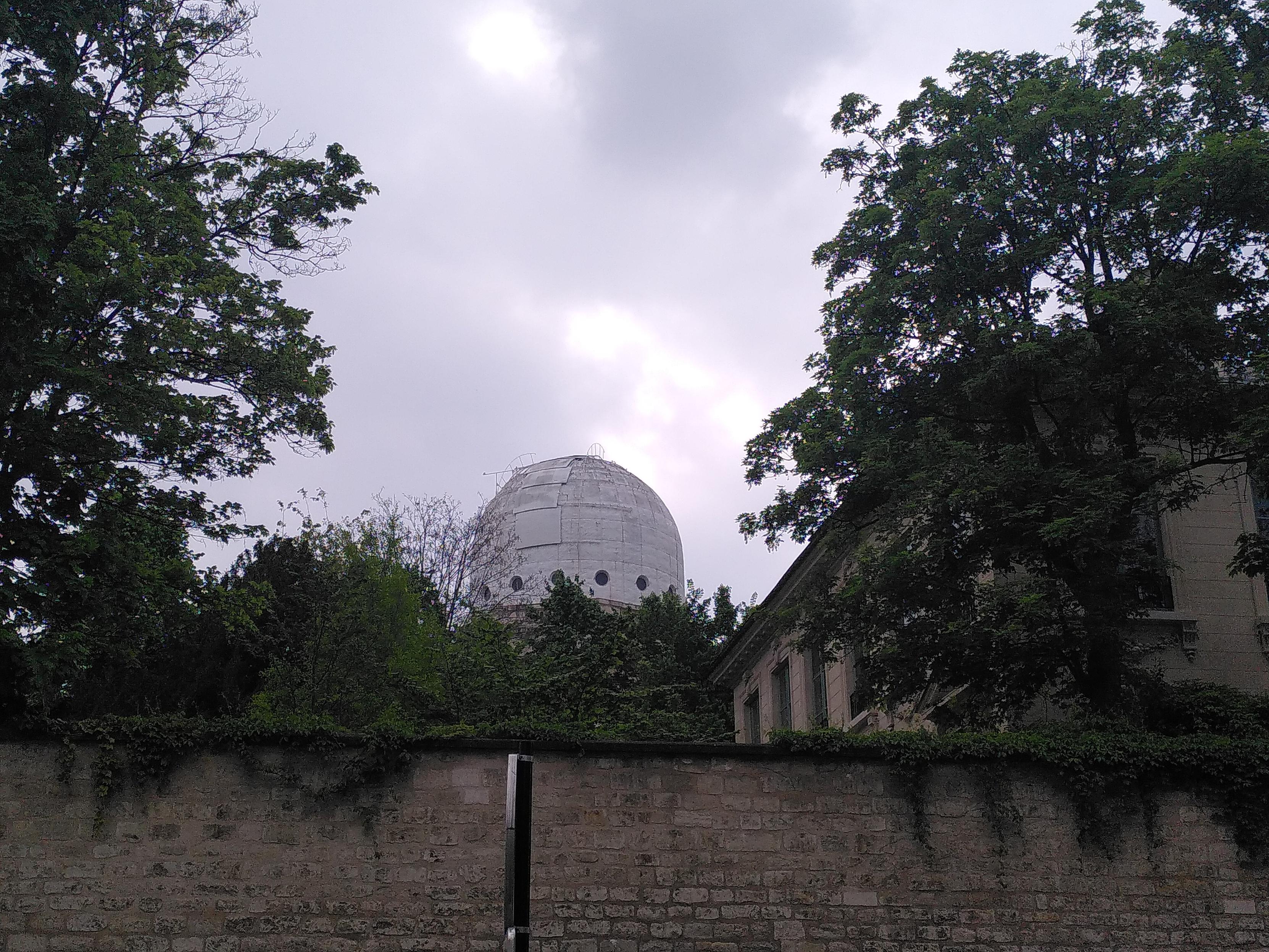 In the far background behind a wall and trees, a dome covered in tarp and white panel. It could be a fake ass observatory