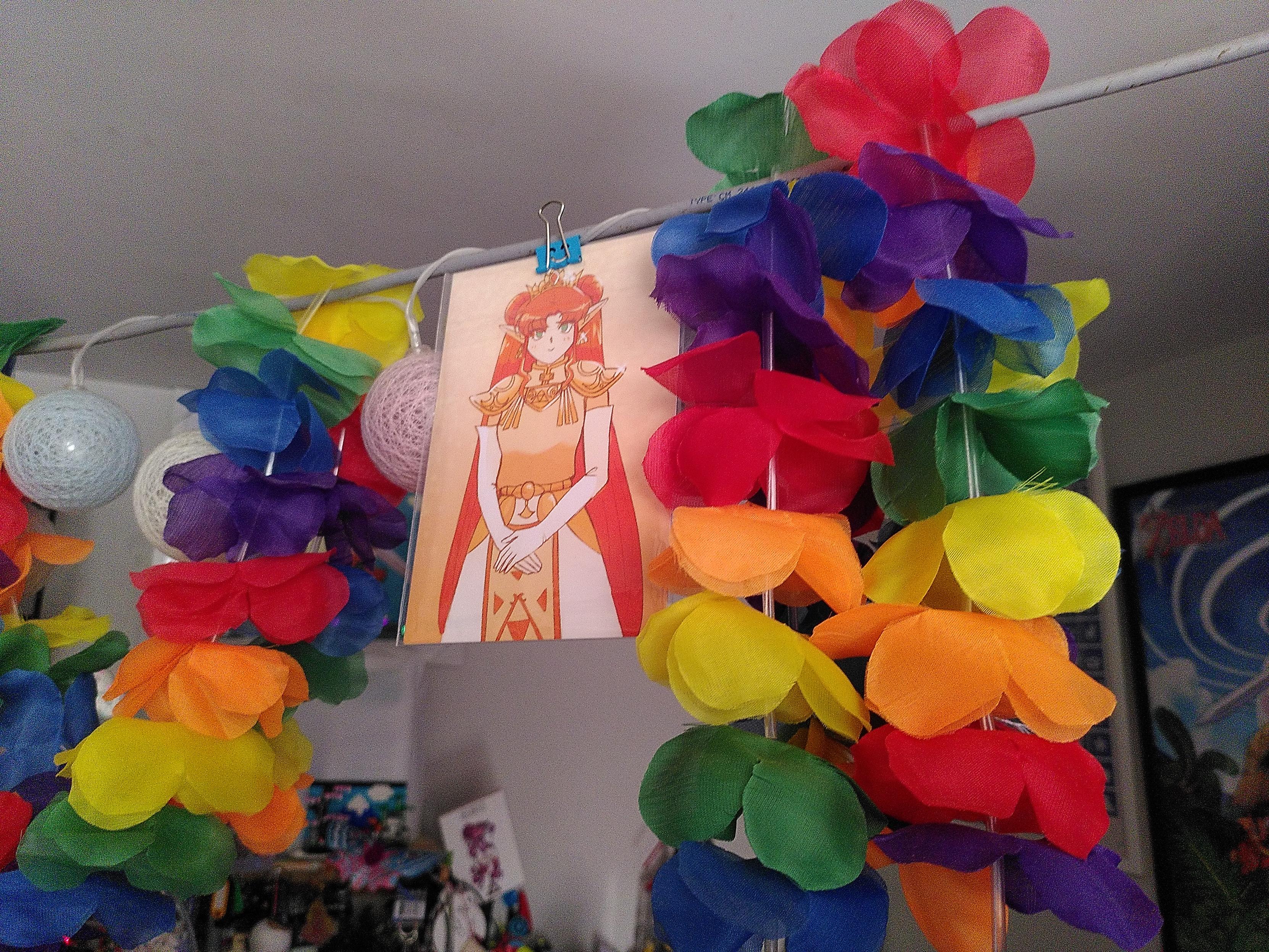 A small print of zelda, in shades of oranges, attached to a suspended rj45 cable alongsode trans-colored lampion and rainbow-colores plastic flower necklace