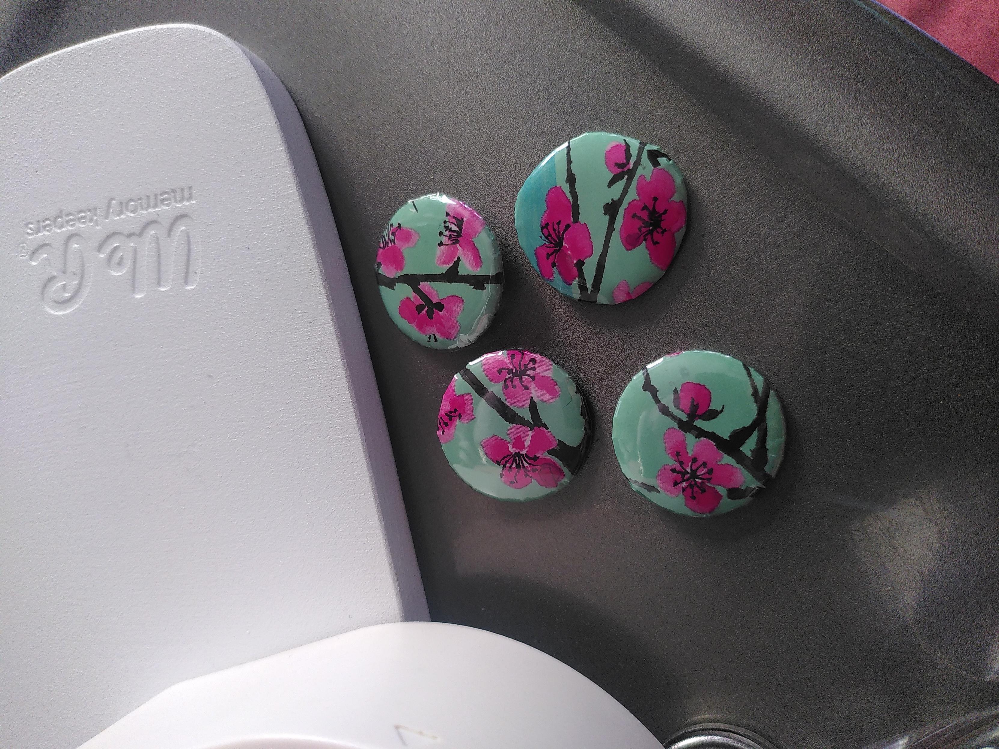 4 badges, 25mm in diameter, sporting pieces of an arizona ice tea bottle as pattern. All four sport an aqua background, dark branch and hot pink cherry flower