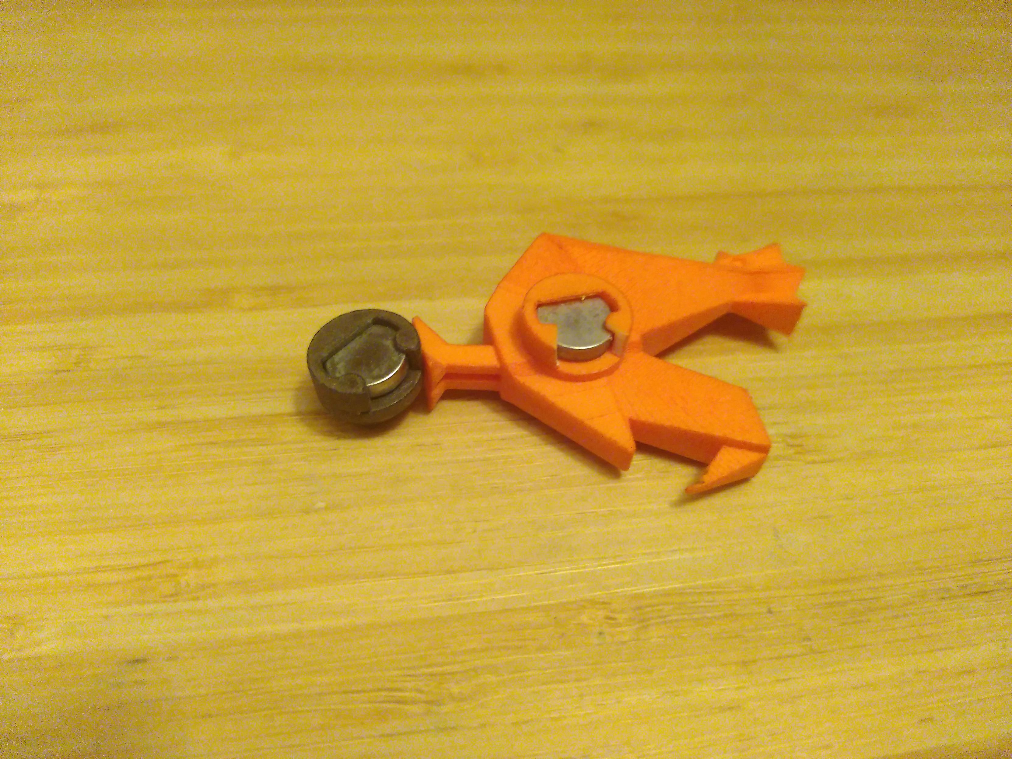 Two 3D print holding coin shaped magnet. One is a black cylinder a couple millimeter larger than magnet. The other is an orange rooster looking like the french tech logo. Both hold the magnet with the mechanism, two prongs that exploit the slight elasticity of the plastic so the magnet can be pushed in then stay in, resulting in something durable and simple.