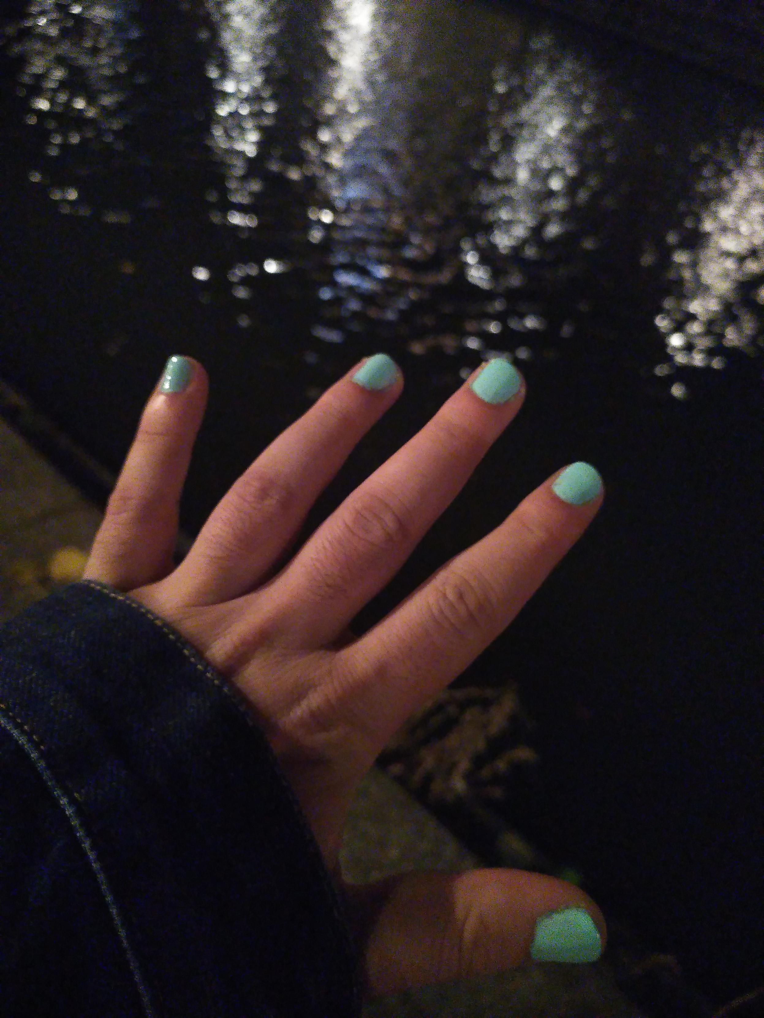 Outdoor night photography of the back of my hand with my nails painted pastel green/aqua. Background is water and reflecting the street lamps