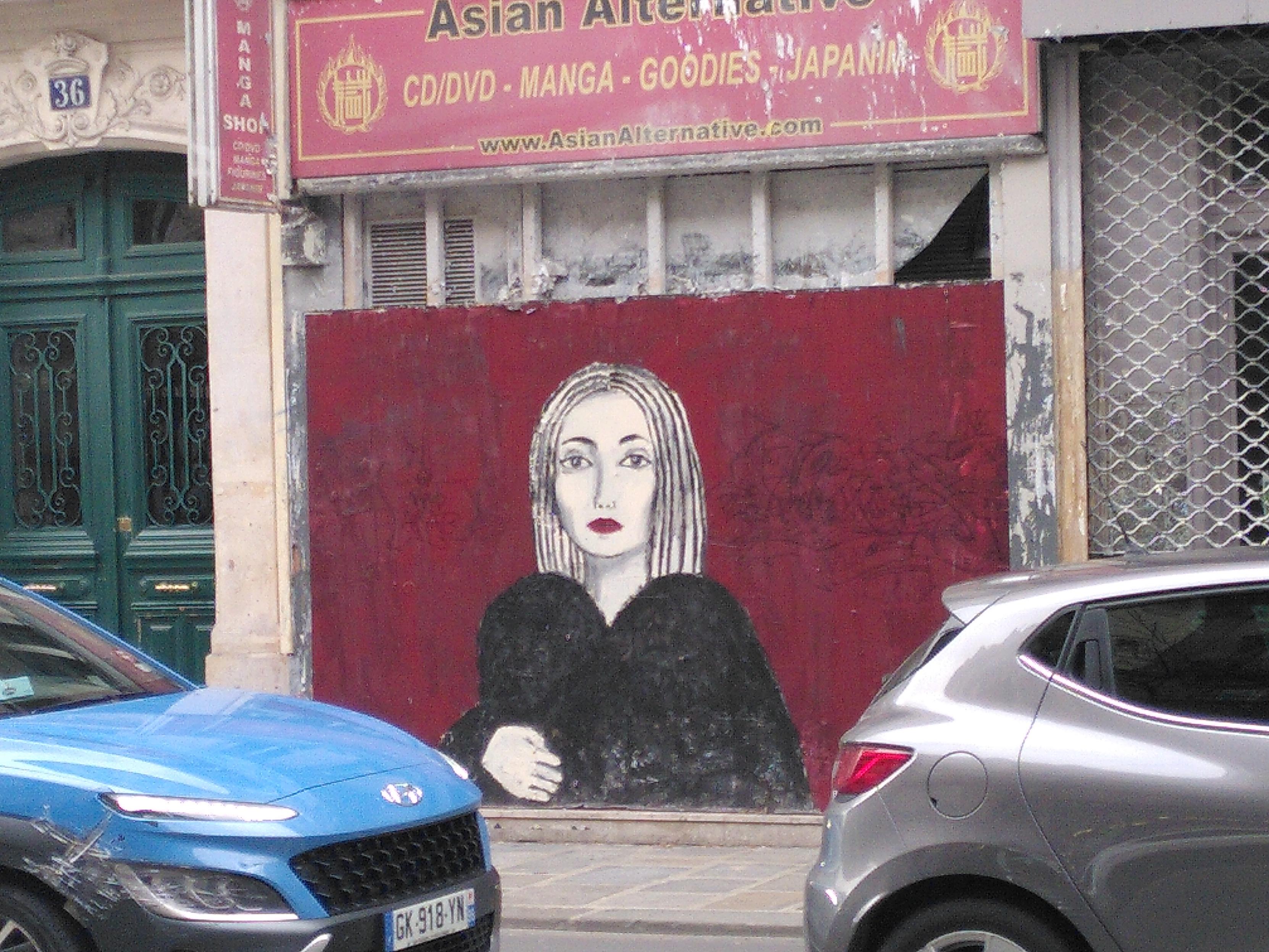 Photo of a piece of street art showing a woman with a black coat in a dark red background