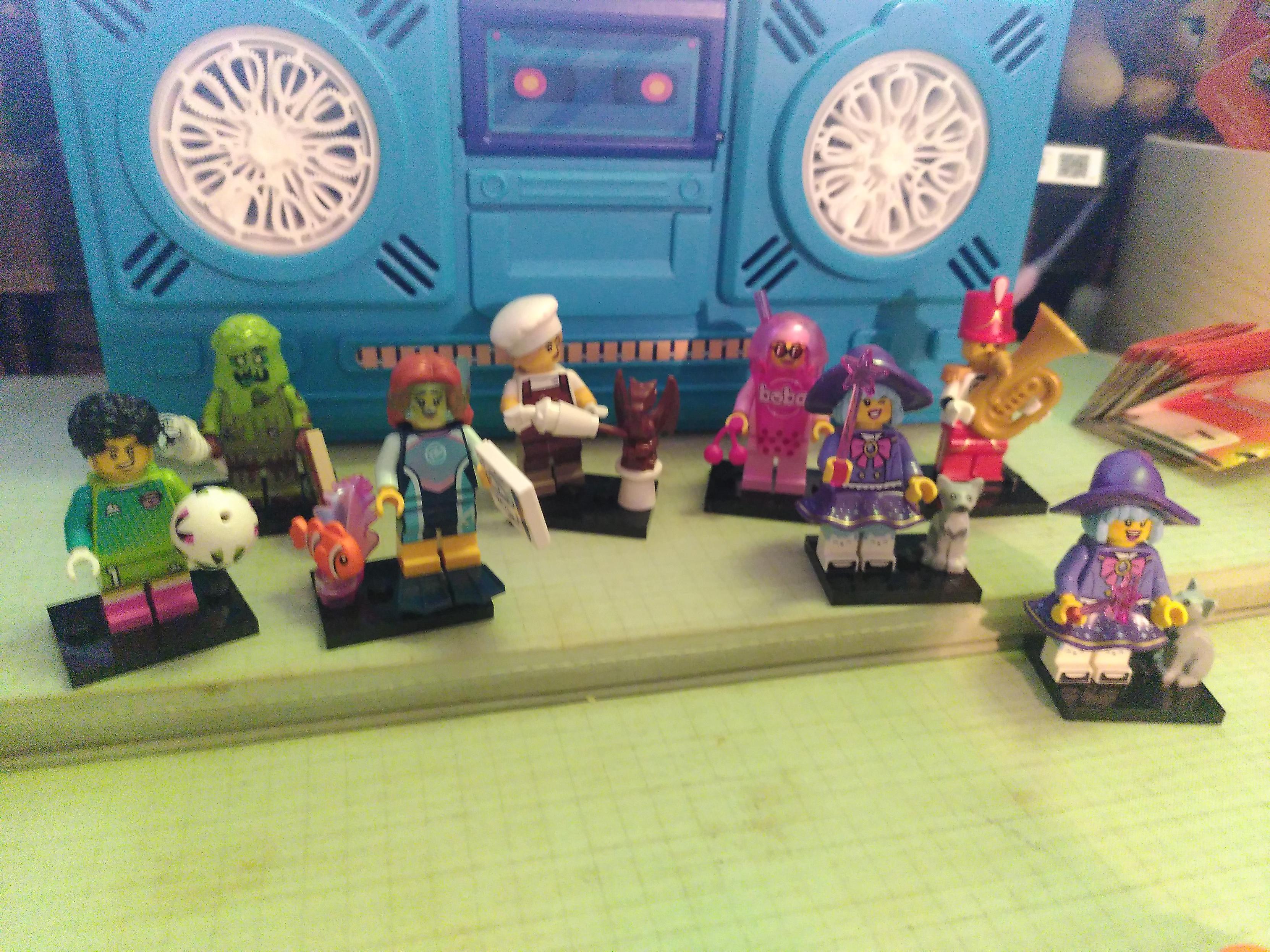 Photo of 8 lego minifigurine (one duplicate) in fronf of a blue machine that make soap bubble, looking like a blue toy boombox 