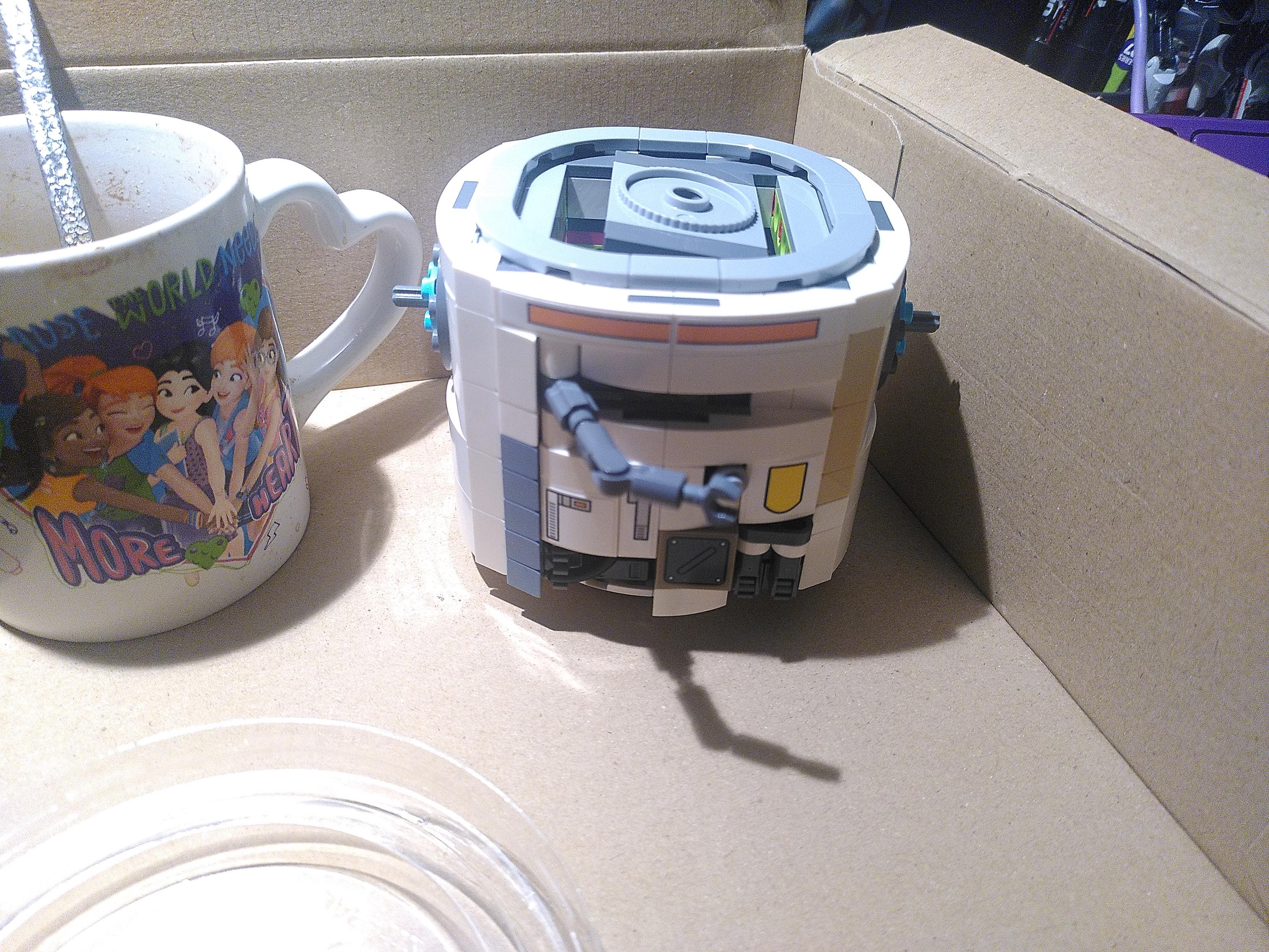 Photo of lego 75416 after bag 3/7. It's a cylinder, white with some grey, orange and yellow, a grey mechanical arm coming from the middle and on top grey circle.
It's sitting in a cardboard box. On the side is a white ceramic lego friend mug saying 
