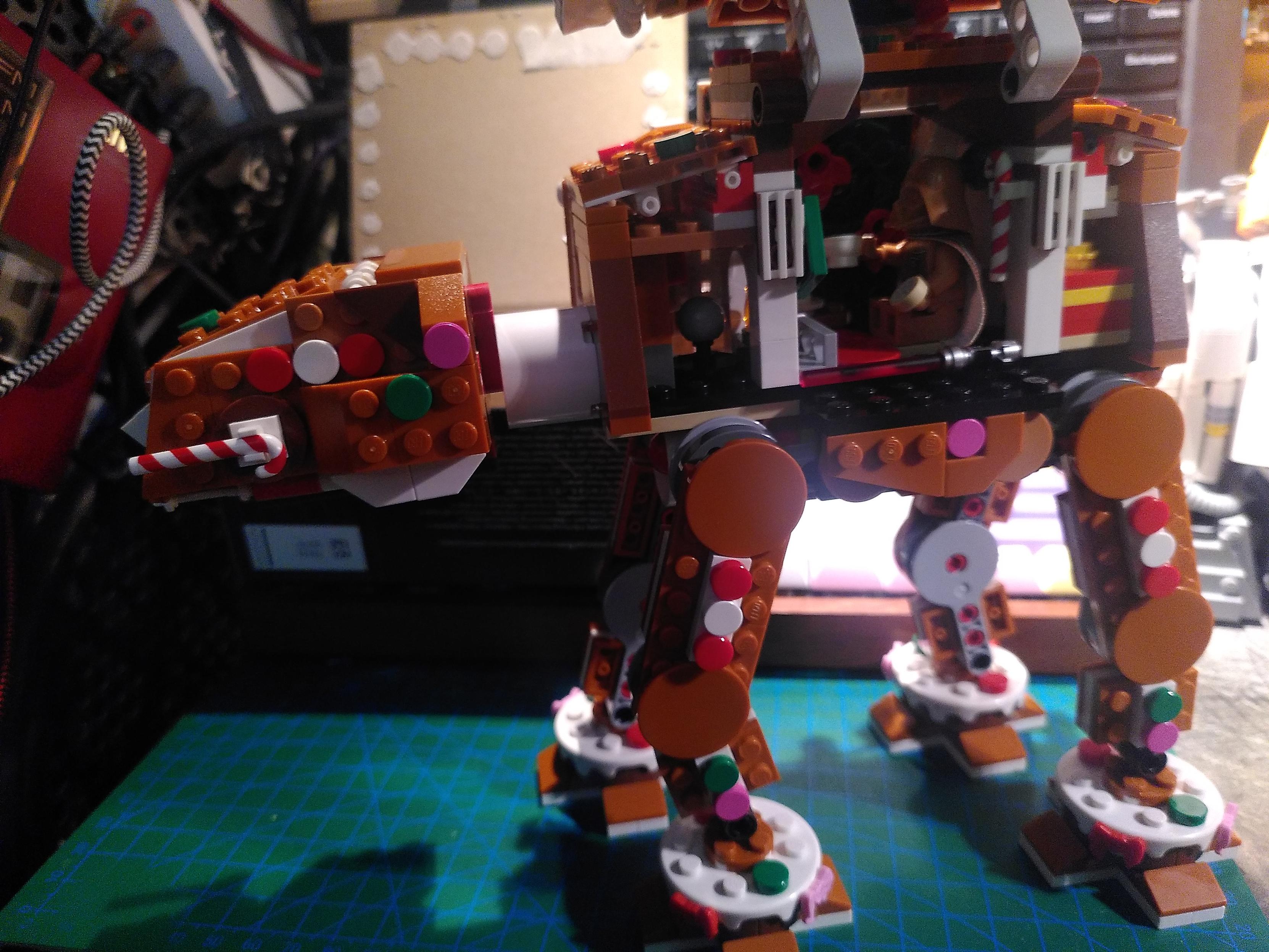 Photo of a lego gingerbread AT-AT. A side panel is open, revealing gingerbread vador sitting with a mug and cookies in front of a fireplace