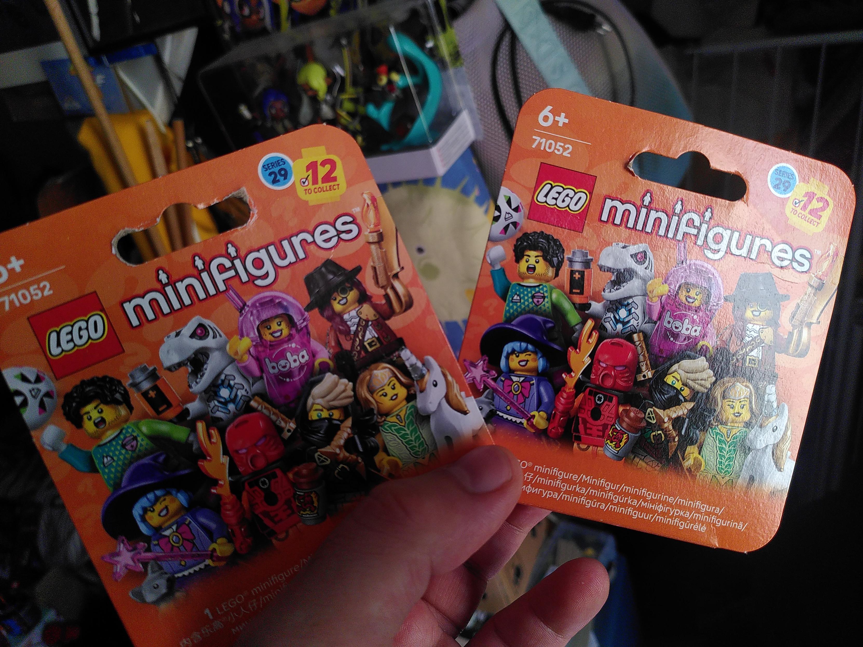 Photo of a hand holding two boxes of lego minifigurine series 29. It's two orange boxea showing 8 minifigurines, a footballer, a robot t-rex, a boba fan, a laxy monster hunter, a cute witch, a bionicle cosplay, a mysterious ronin and a elf lady with a unicorn