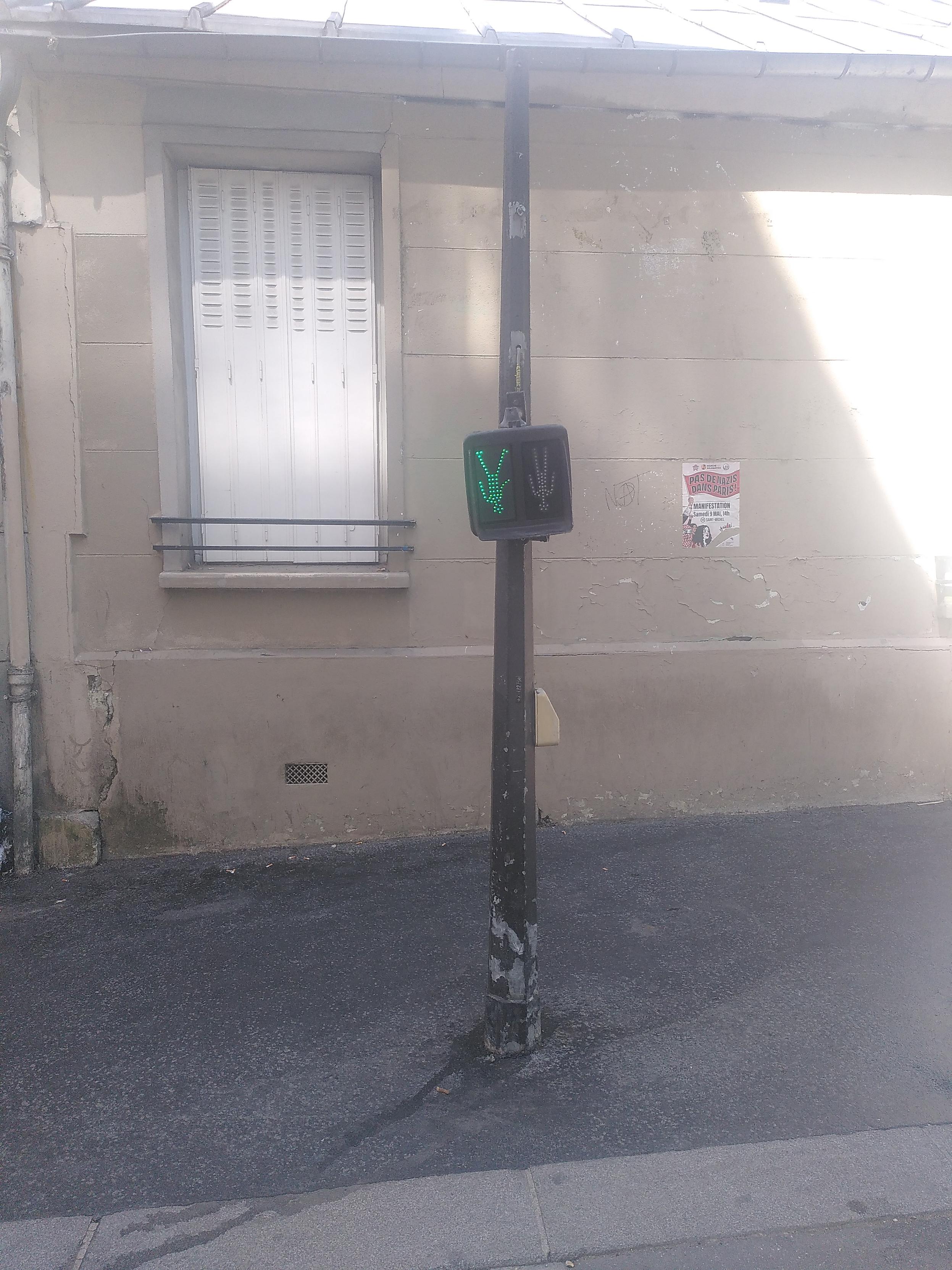 Photo of a post with pedestrian go/no go light. The light's support is broken and it's hanging by its cable. It's showing an upside down green man