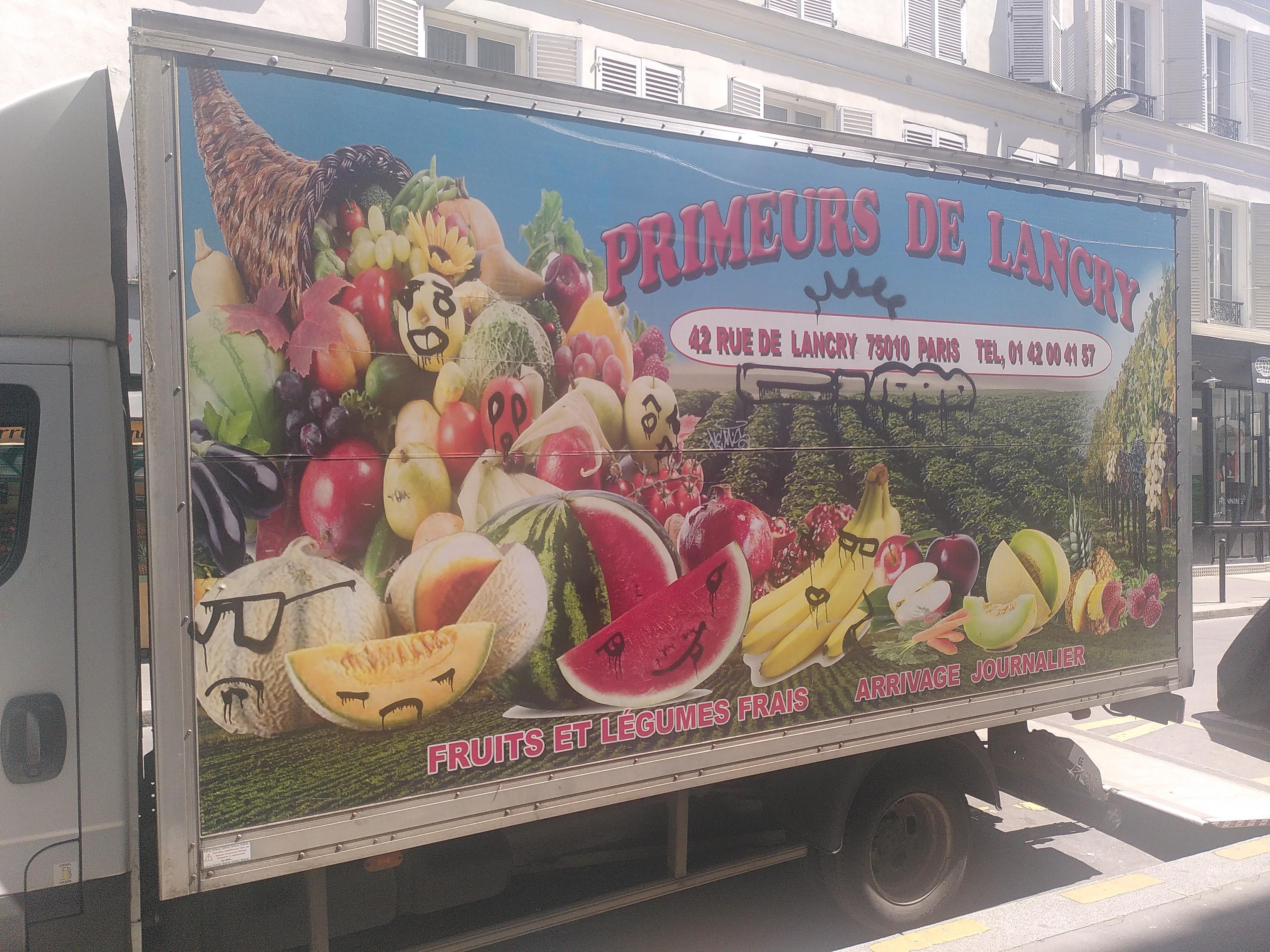 Photo of the side of a mid-sized truck. It's illustrated with a mountain of fruits and veggies, some already cut open like a watermelon. On a bunch of them, face have been spray-painted