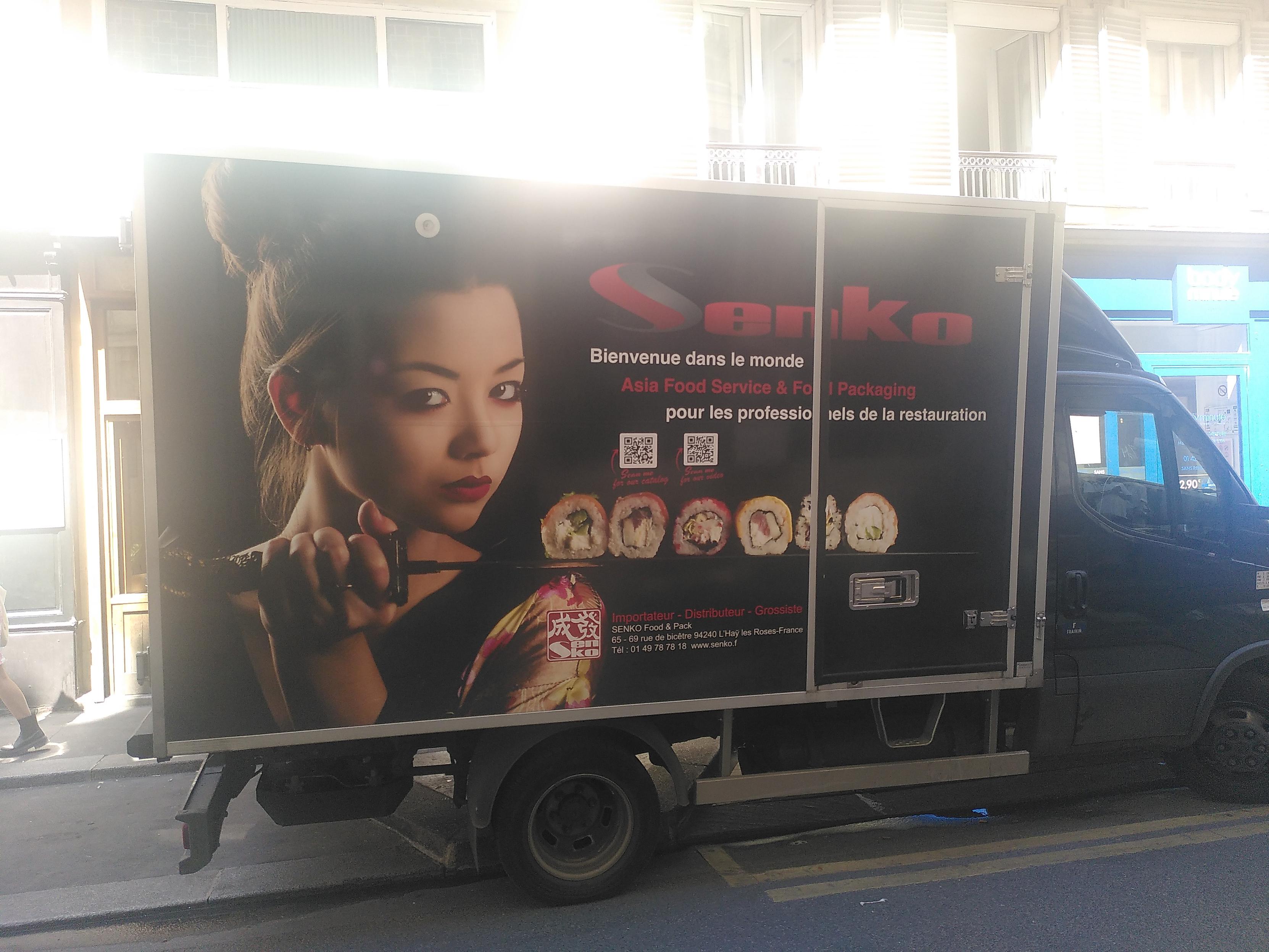 Photo of a mid-sized transport truck. It's decorated with an asian woman holding a katana and on top of the blade are 6 maki